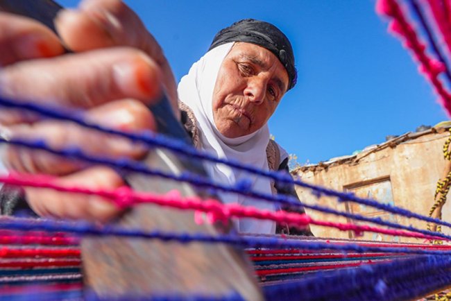 Evinin bahçesindeki tezgahta asırlık yöntemle kilim dokuyor
